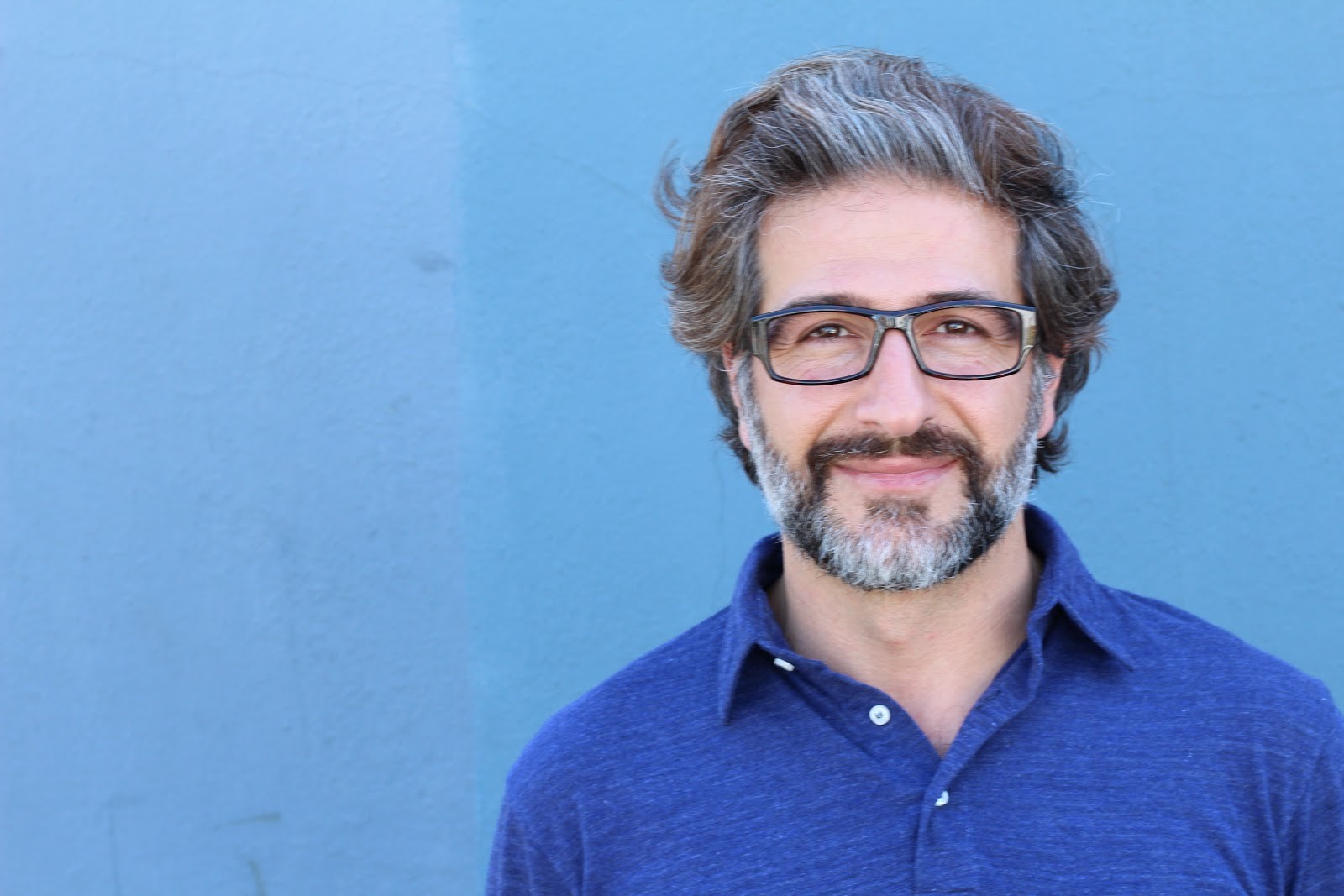 Man with beard and glasses wearing blue polo shirt against blue background