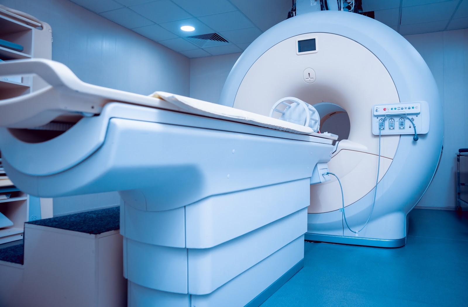Modern MRI scanner in a blue hospital room with patient table and control panel
