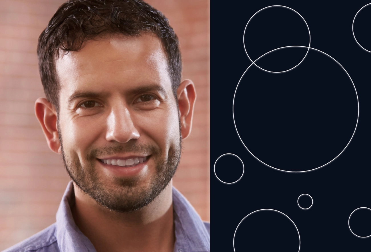 Man with beard smiling next to abstract white circles on dark background