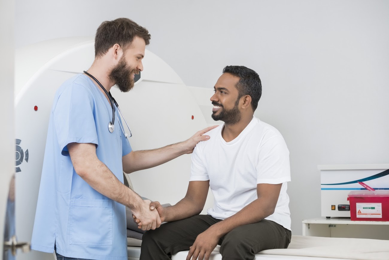 Medical worker smiling and shaking hands with the patient sitting on the MRI machine