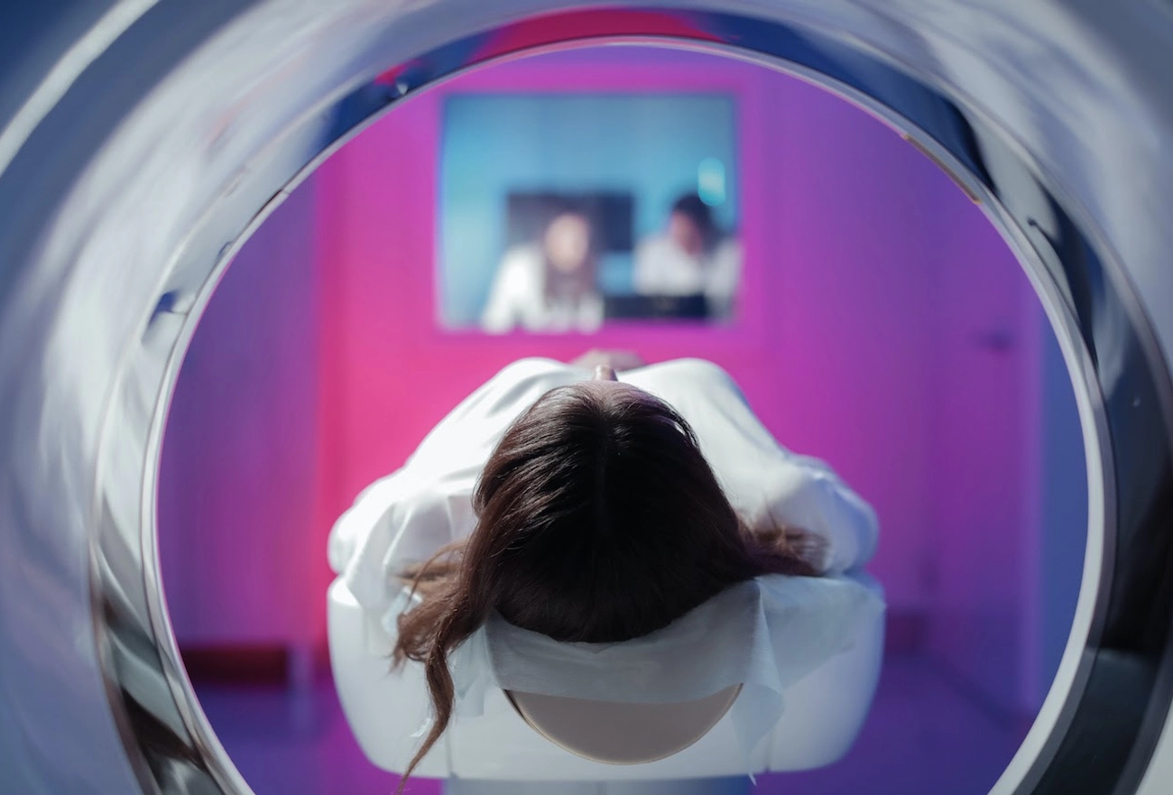 Woman laying inside of an MRI machine while doctors are looking through the window from the operating room