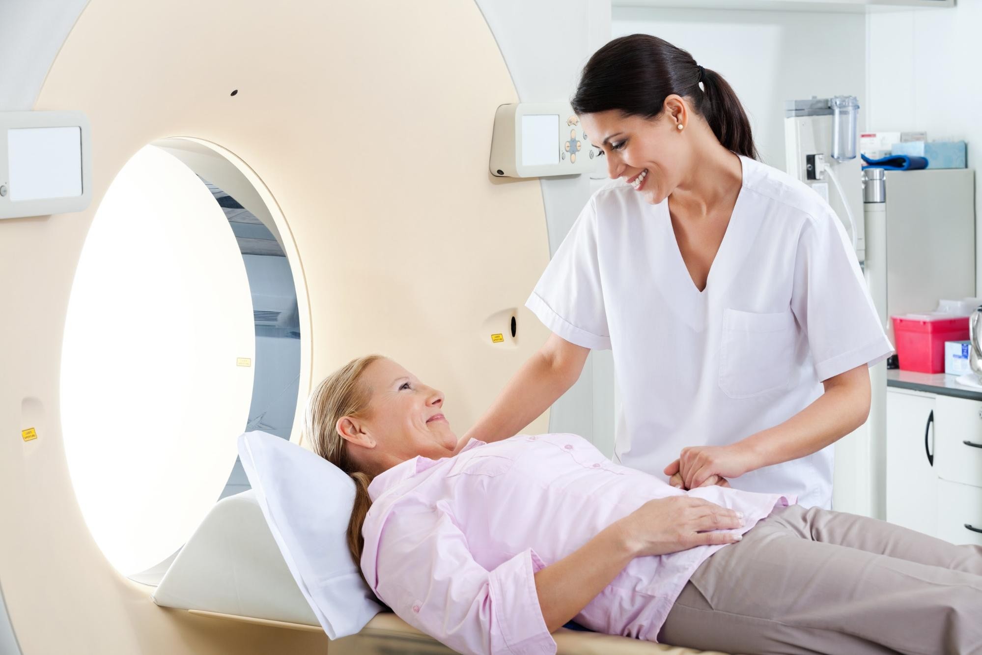 Patient lying on medical imaging scanner with technician assisting during scan procedure