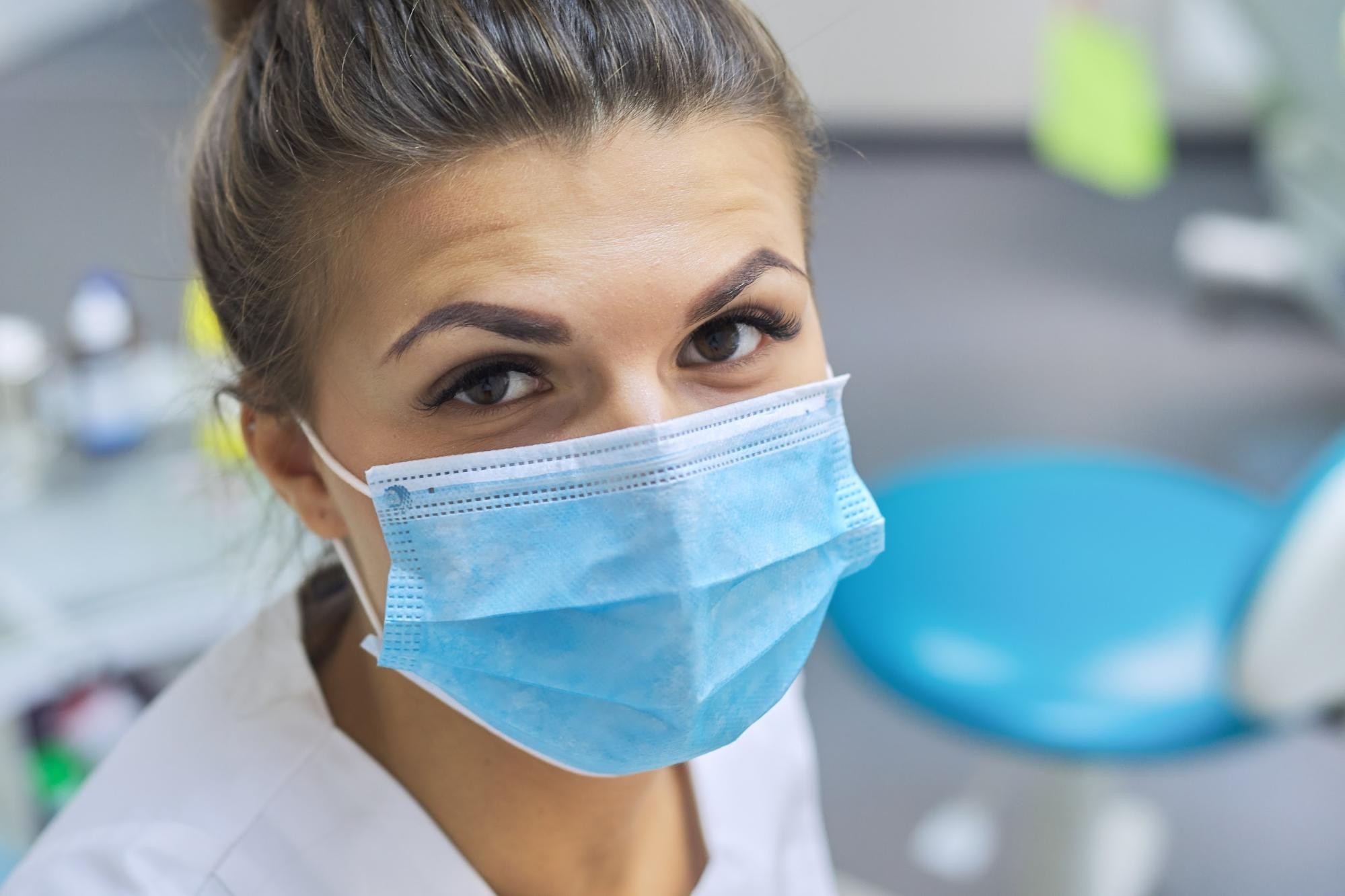 Woman wearing blue surgical mask in medical setting looking at camera