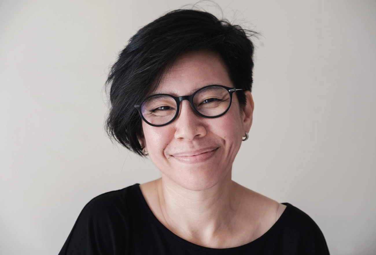 Person with short black hair and black-rimmed glasses wearing black shirt smiling at camera