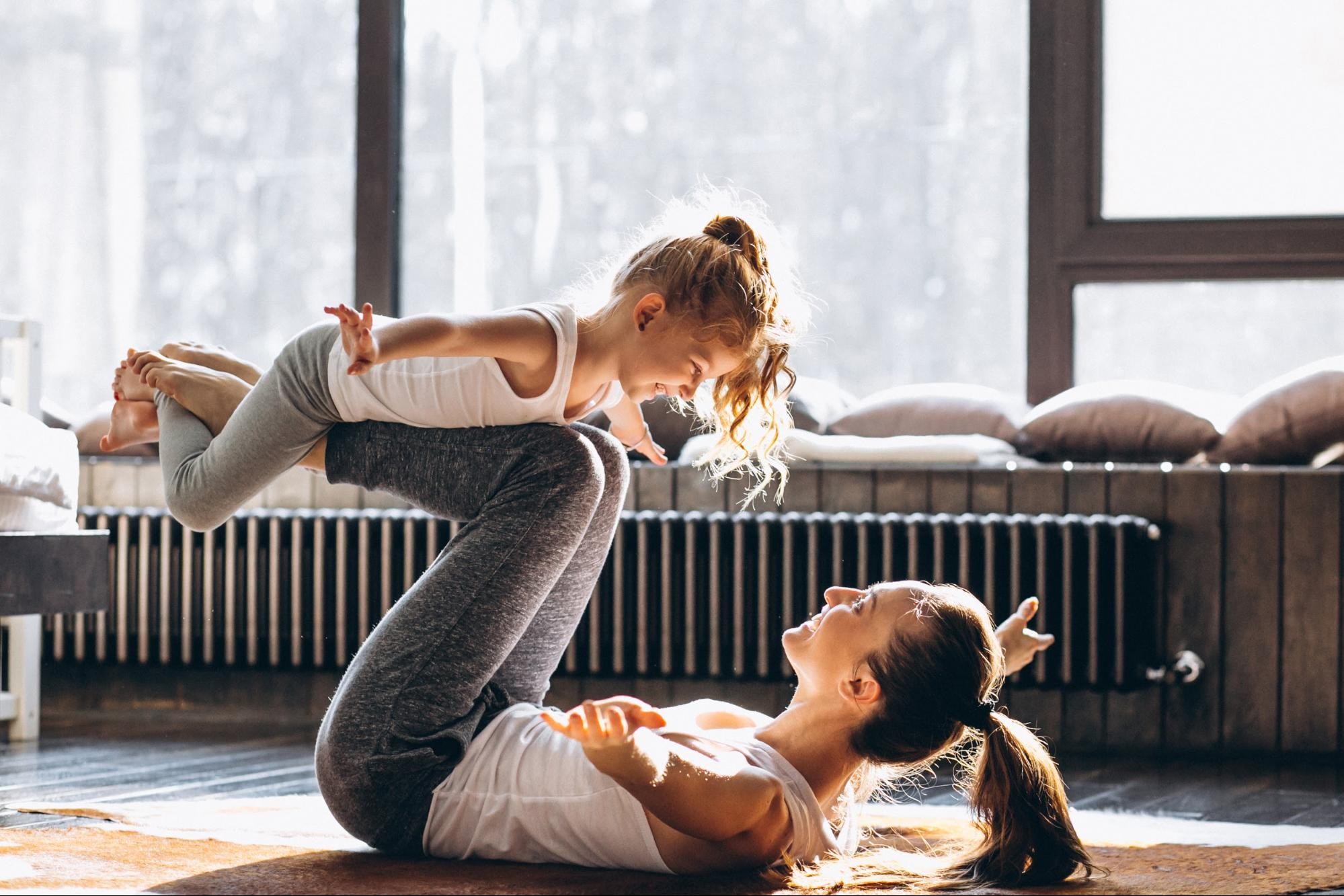 Women doing a yoga pose with her daughter in bright loft space with large windows and natural sunlight