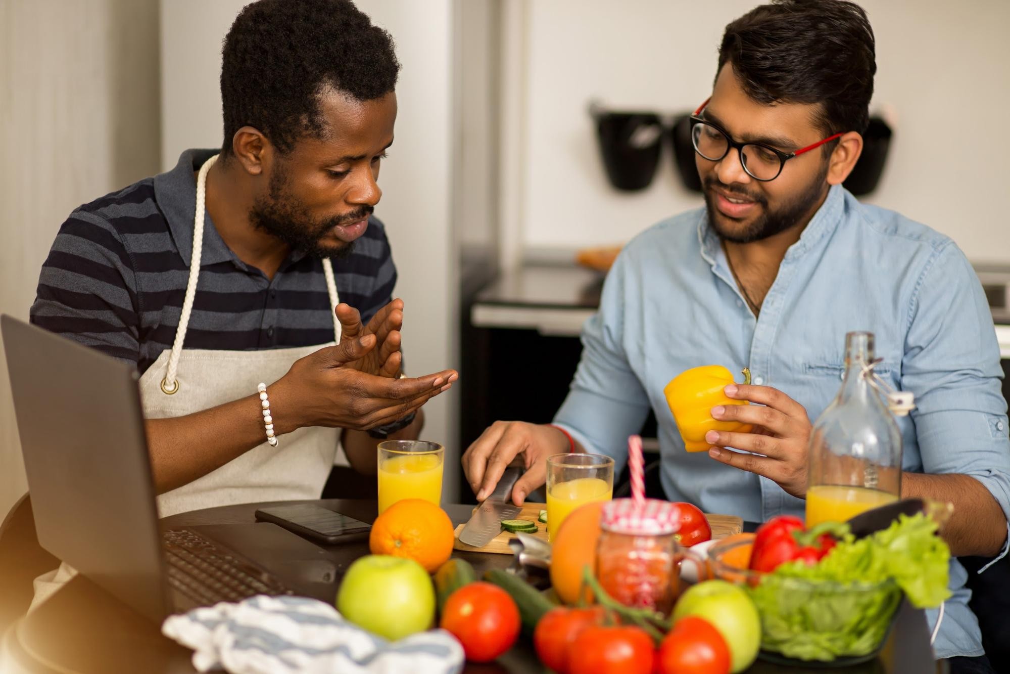 Two men discussing healthy eating with fresh produce and juice at kitchen table