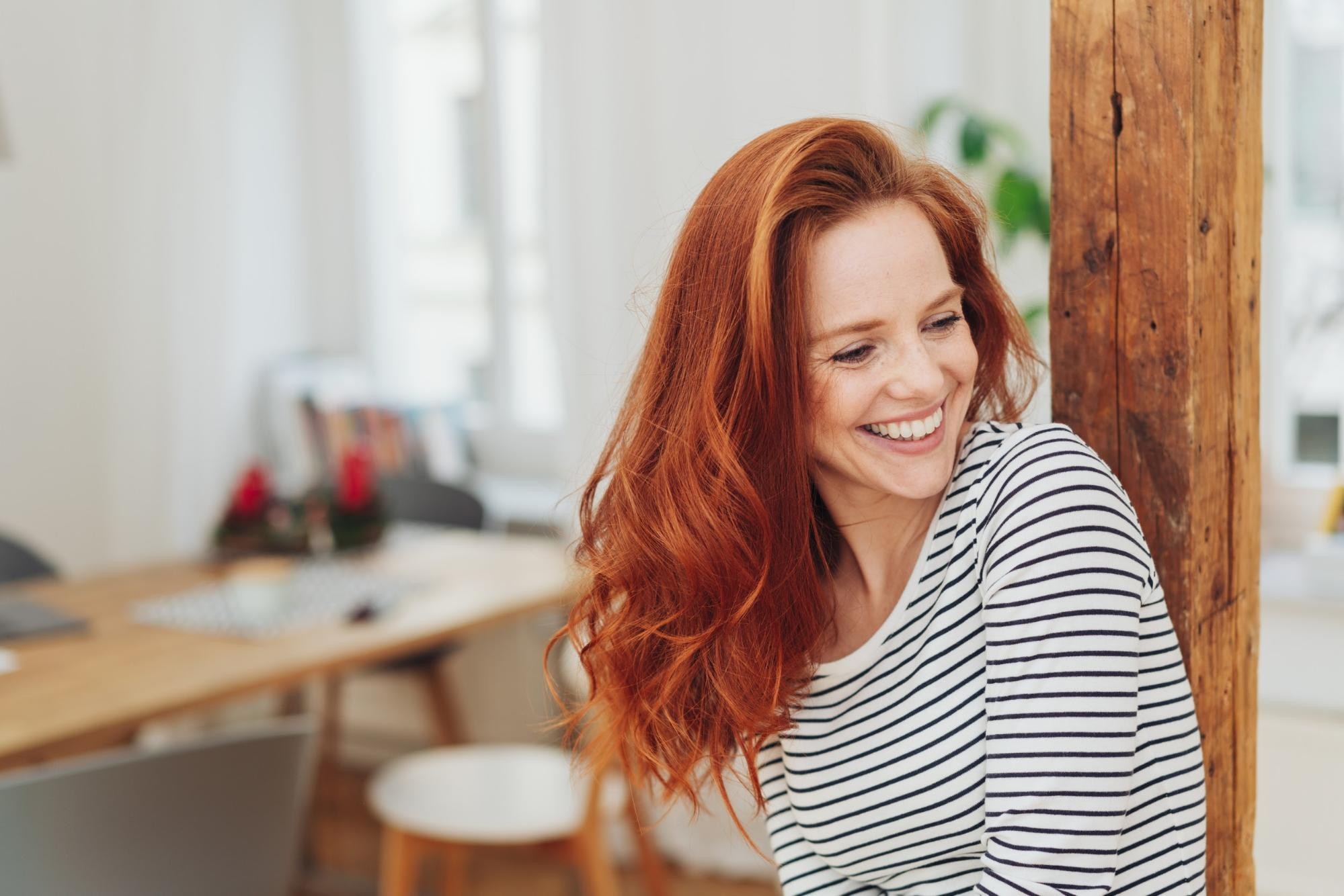 Woman with red hair in striped shirt smiling in modern office space