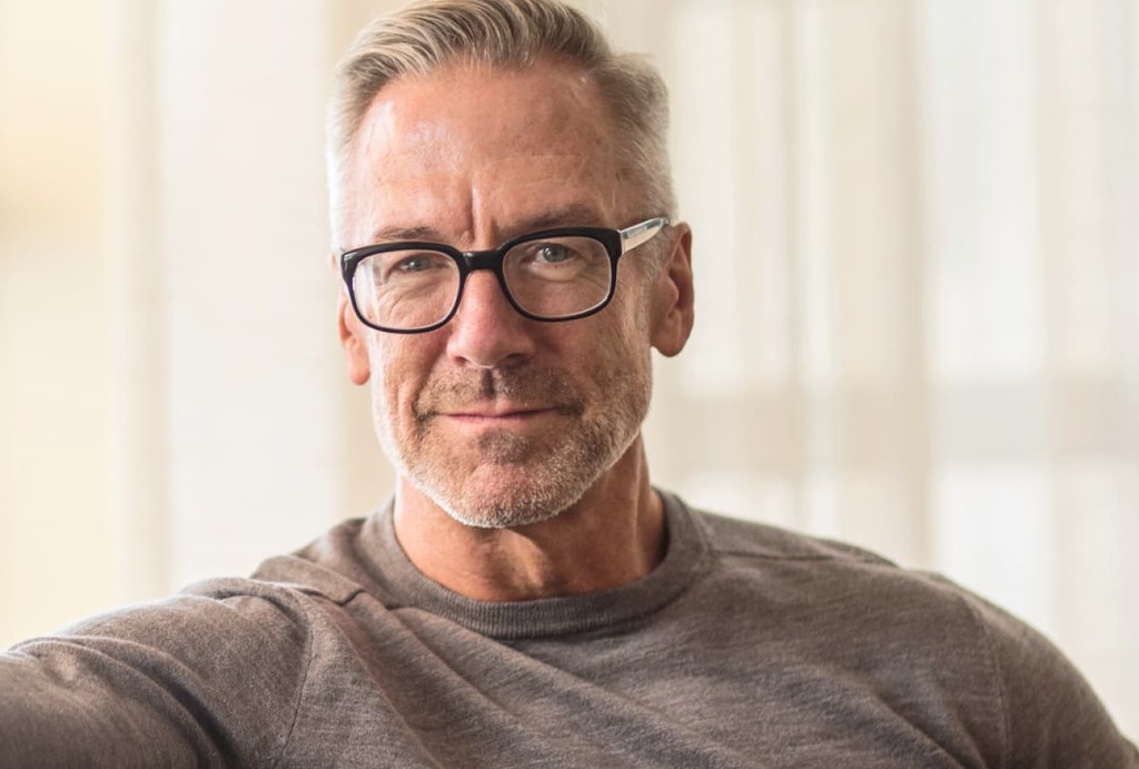 Middle-aged man with gray hair and glasses wearing gray shirt in indoor setting