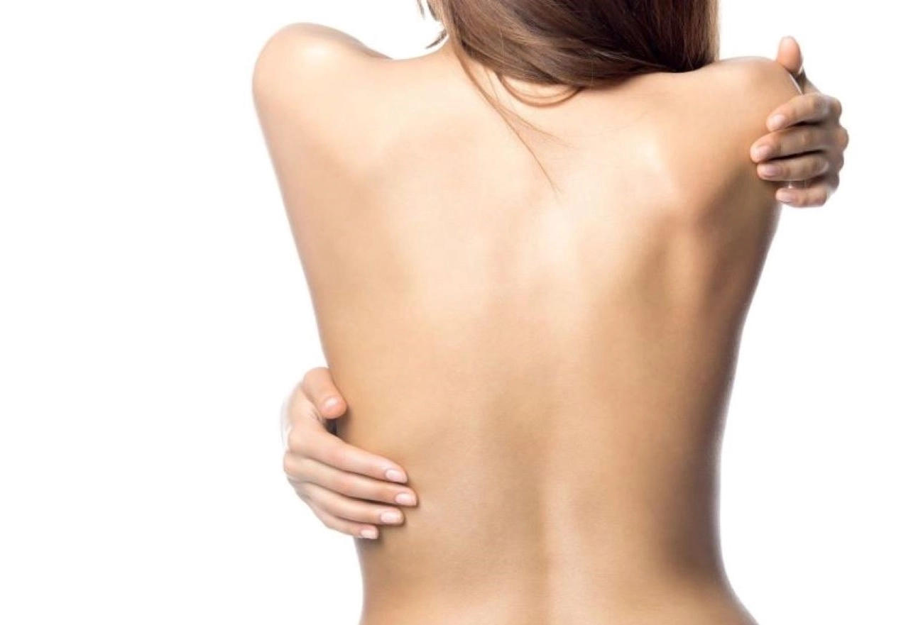 Woman shown from behind touching her back to indicate pain or body examination area