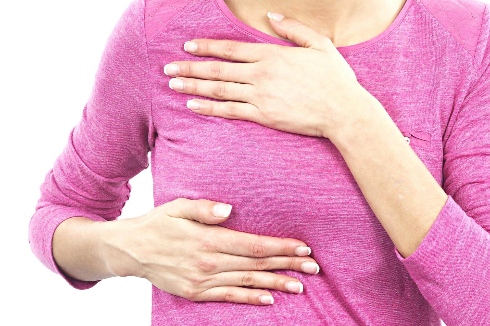 Person in pink long-sleeved shirt with both hands placed on chest area against white background