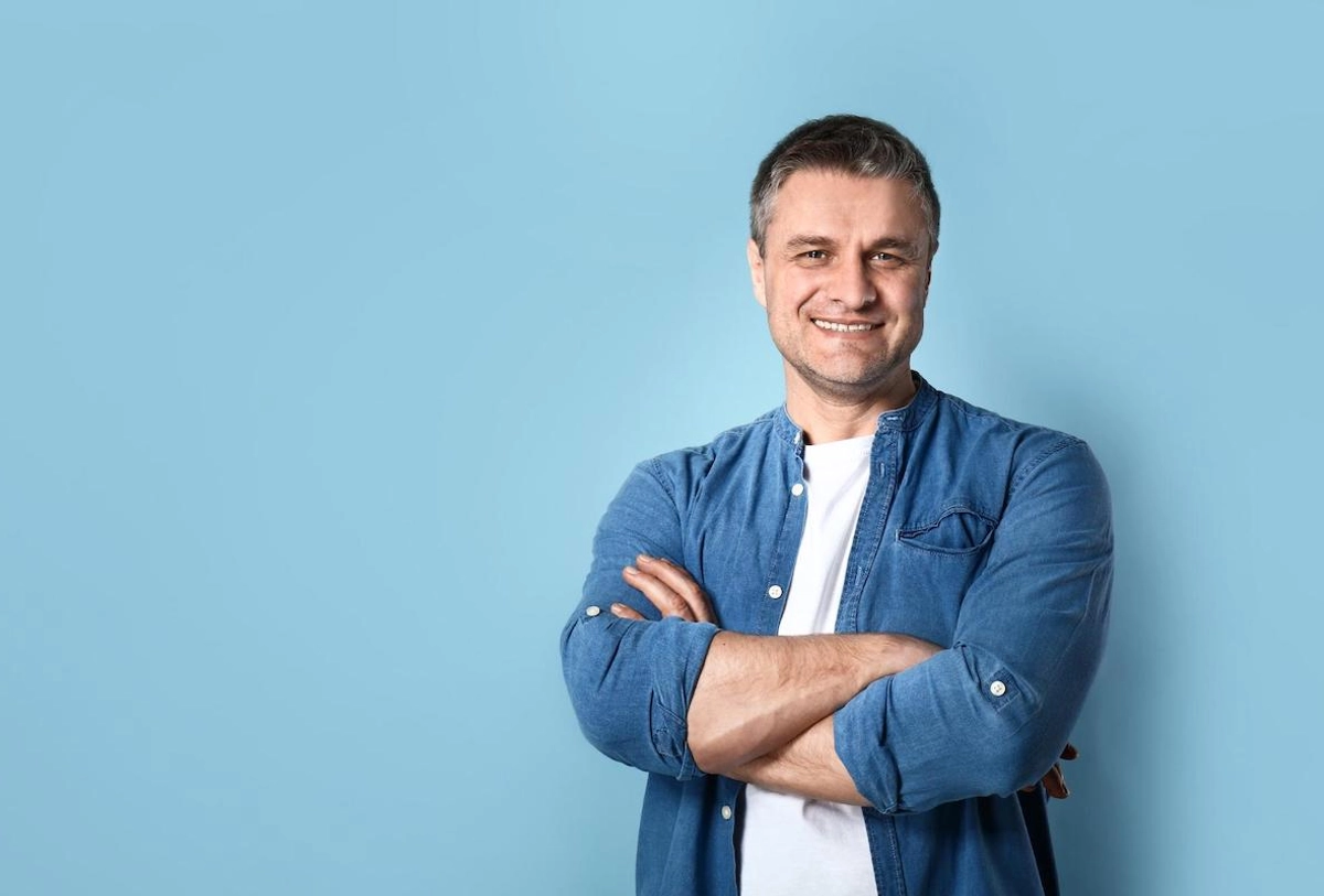 Man in blue denim shirt with arms crossed smiling against blue background