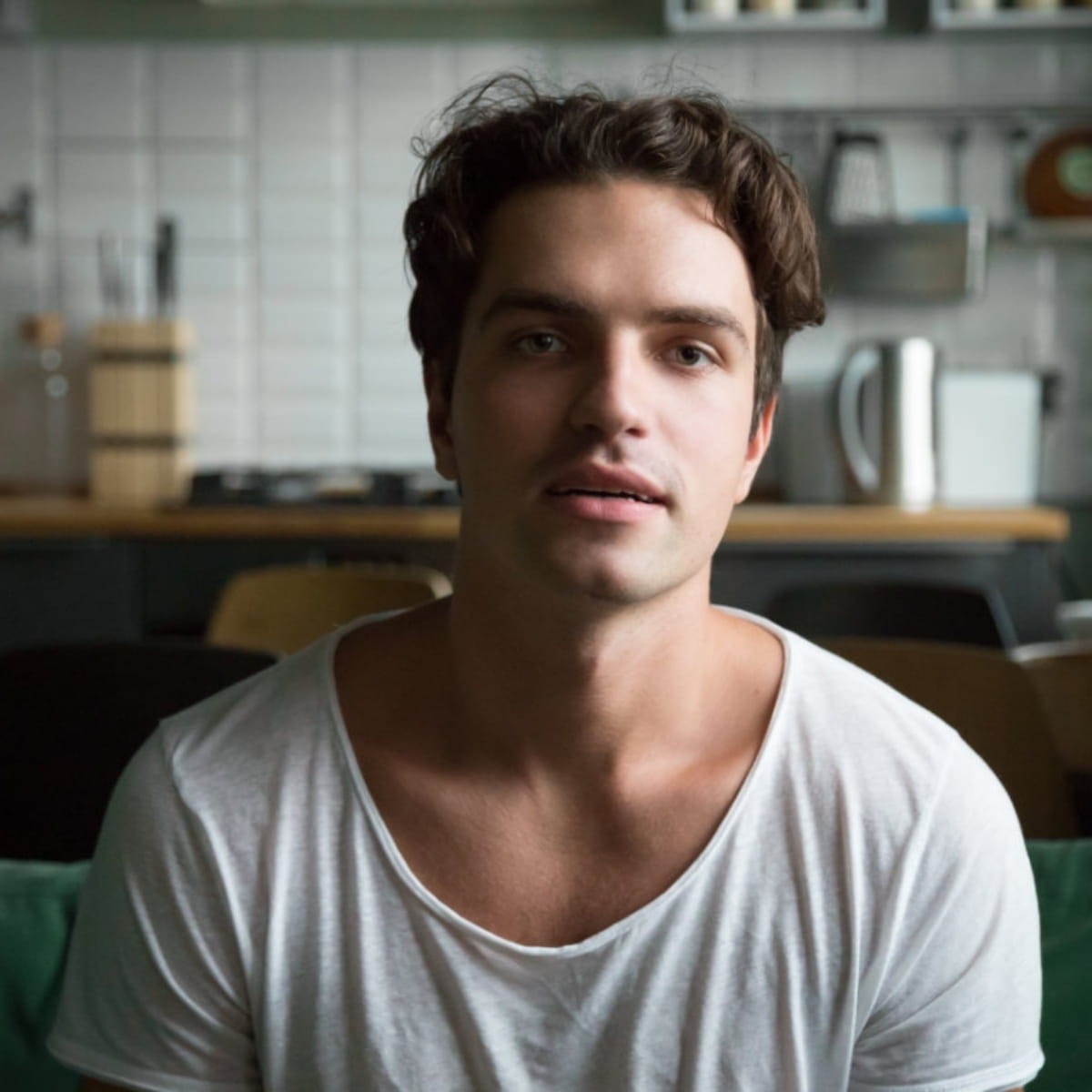 Man in white t-shirt looking at camera in modern kitchen with tiled walls