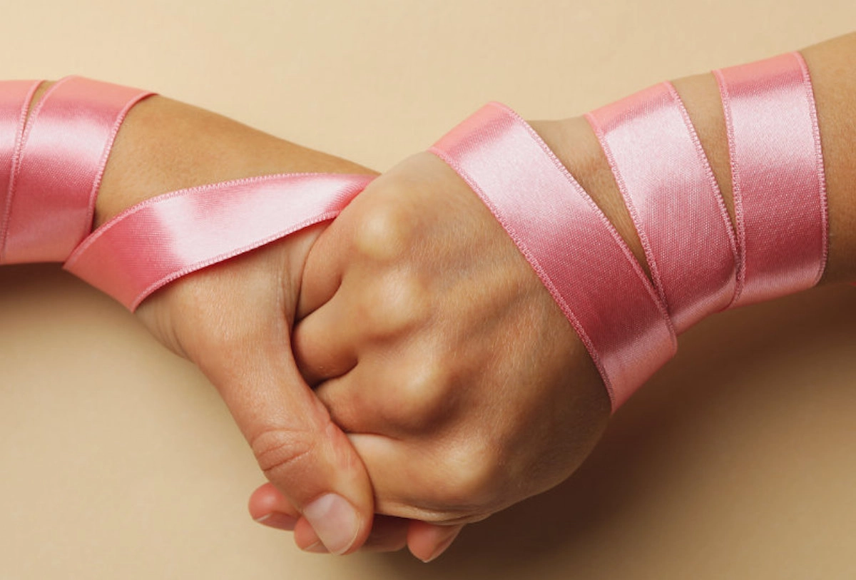 Adult and child's hands joined with pink ribbons representing unity and support