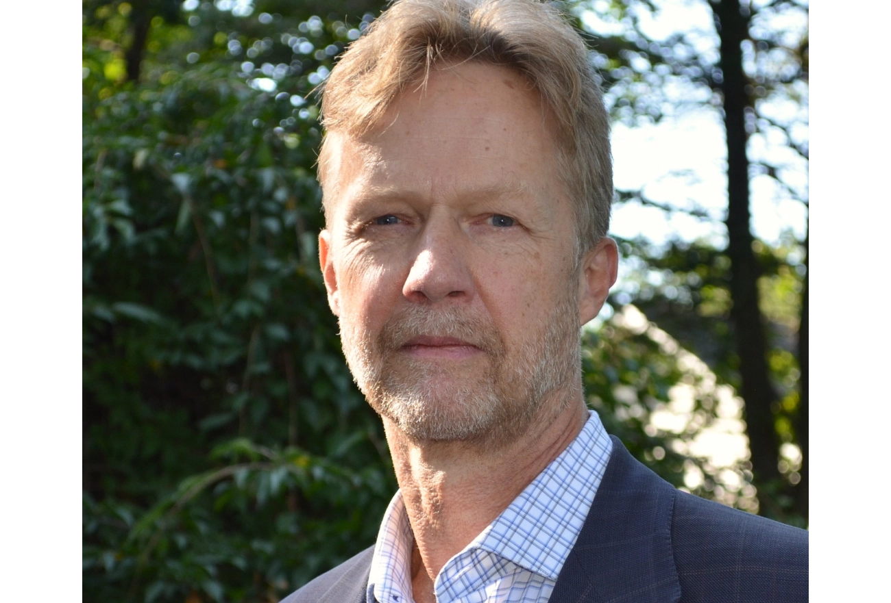 Middle-aged man with gray hair and beard wearing navy blazer and checkered shirt outdoors