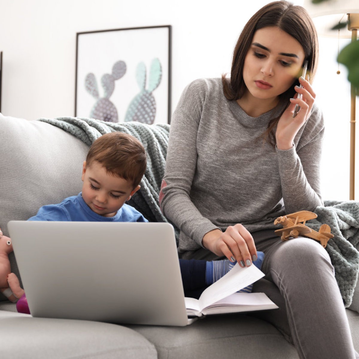 Woman and young child sitting on couch working together on laptop with book in modern living room