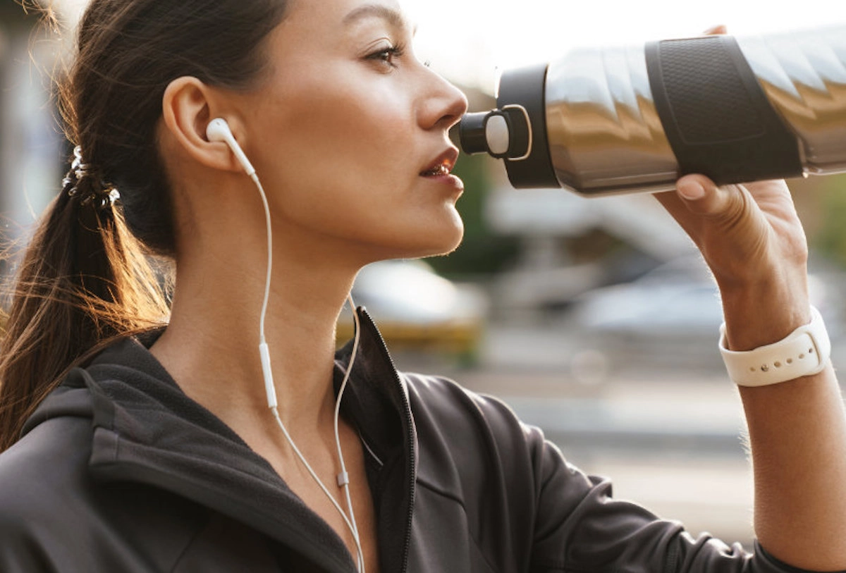 Woman in black jacket wearing earbuds peers through binoculars on city street