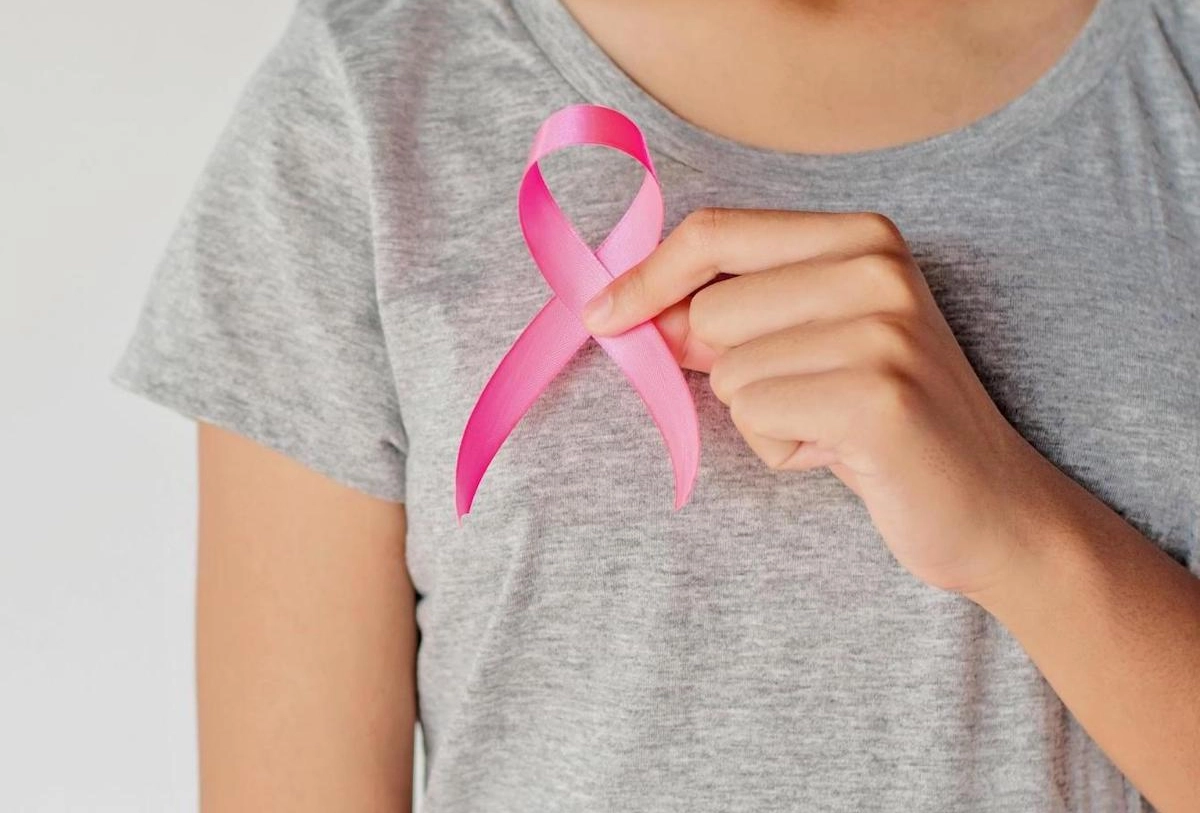 Person in gray shirt holding pink breast cancer awareness ribbon