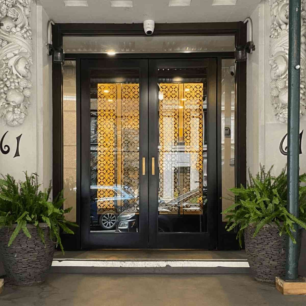 Elegant building entrance with black double doors, gold lattice panels, and decorative ferns flanking ornate stone facade