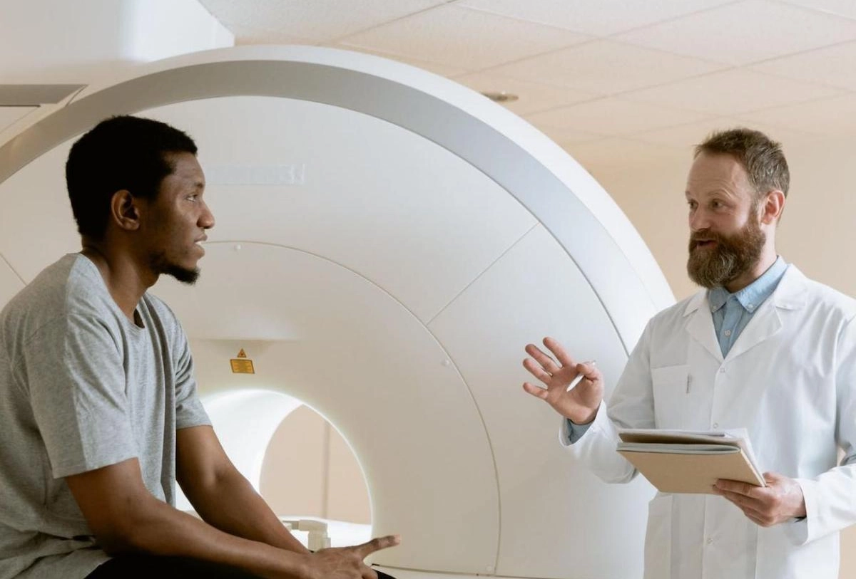 Doctor explaining MRI scan results to patient holding tablet in front of MRI machine