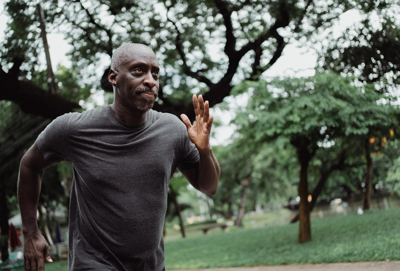 Man jogging in park wearing gray t-shirt with trees in background during outdoor exercise
