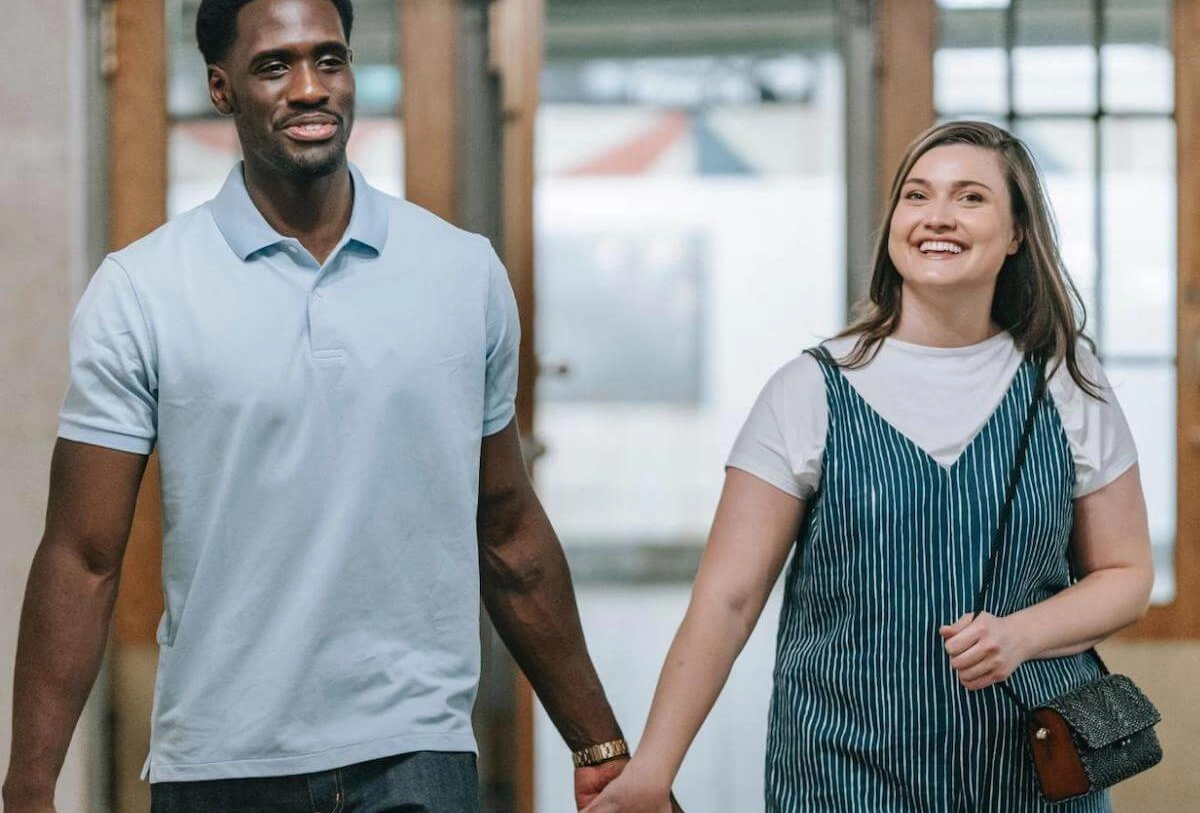 Smiling couple holding hands walking together through modern office building with glass walls