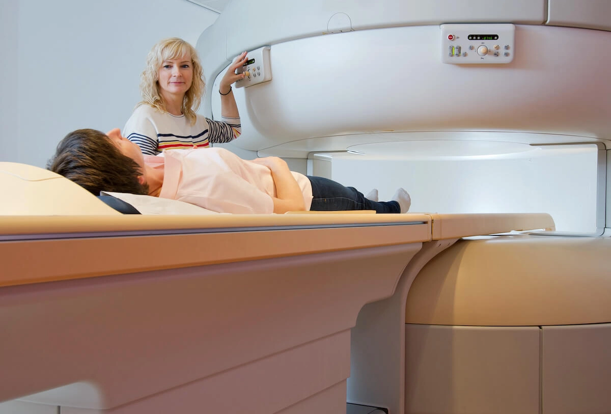 Female technician operating MRI scanner controls while child patient lies inside machine for diagnostic imaging