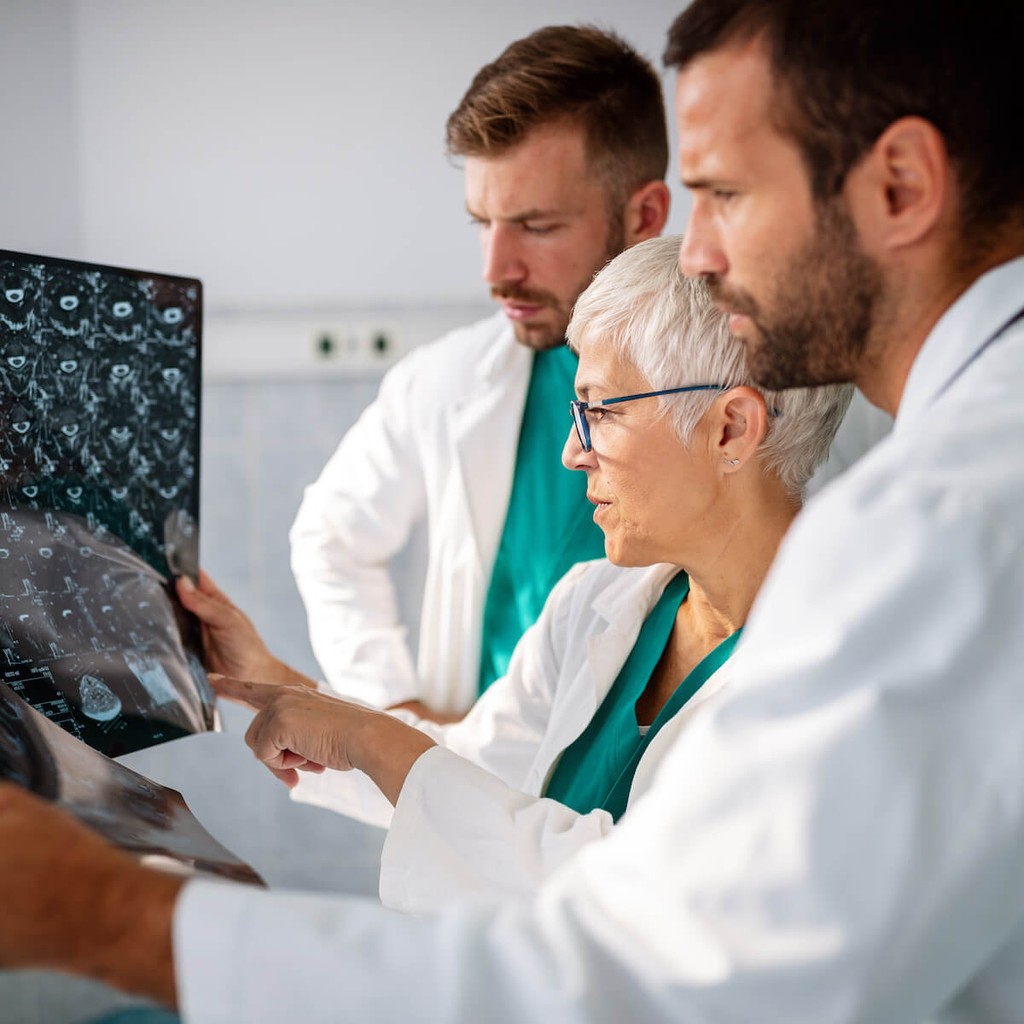 Three healthcare professionals reviewing medical imaging scans, including woman in green scrubs and two men in white coats