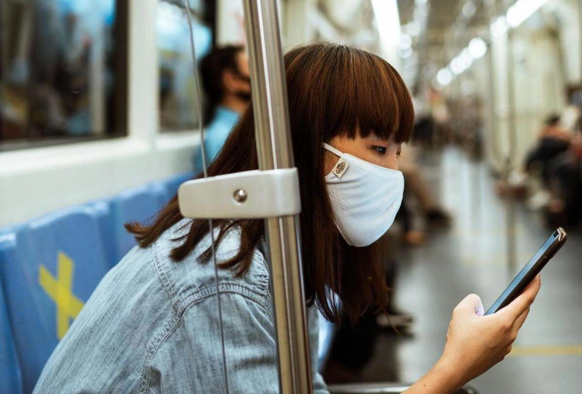 Woman wearing face mask on public transit holding smartphone