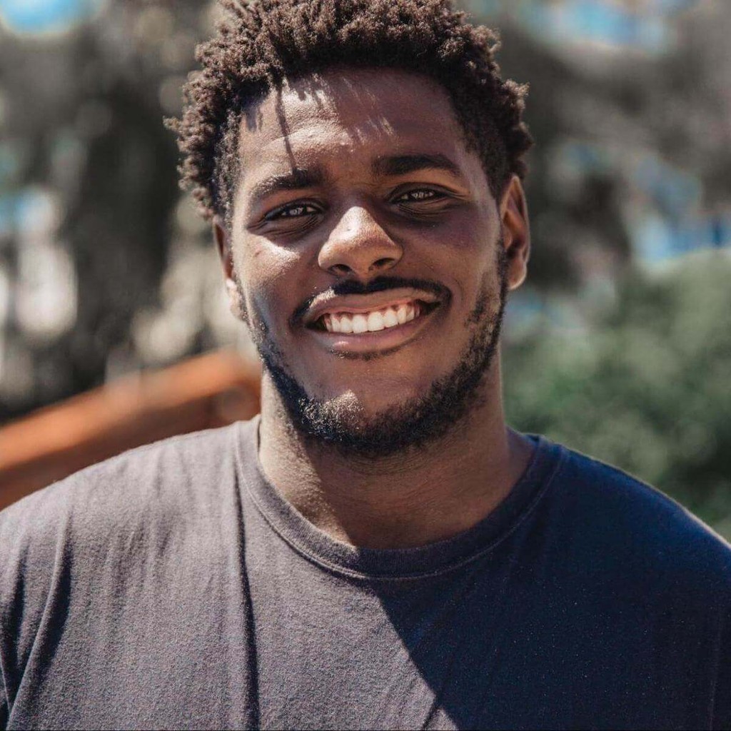 Smiling man in dark shirt outdoors with blurred background
