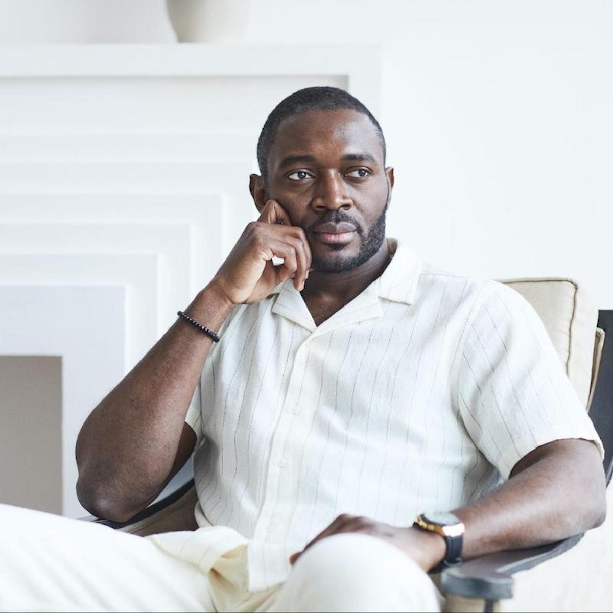 Man in white pinstriped shirt sitting with hand to face in thoughtful pose indoors