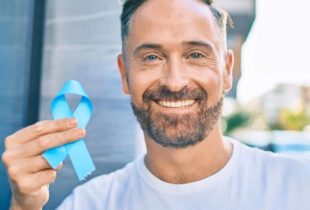 Smiling man holding light blue prostate cancer awareness ribbon outdoors