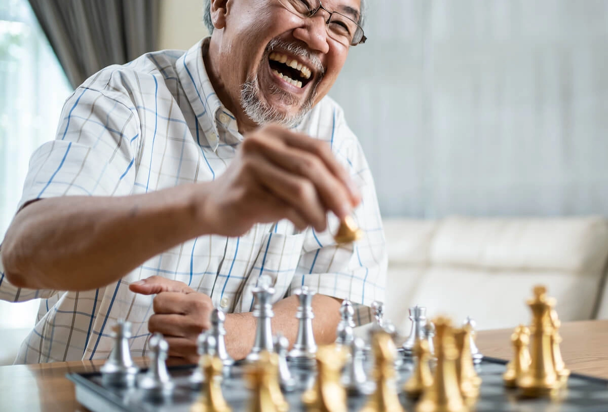 Senior man laughing while playing chess at table indoors