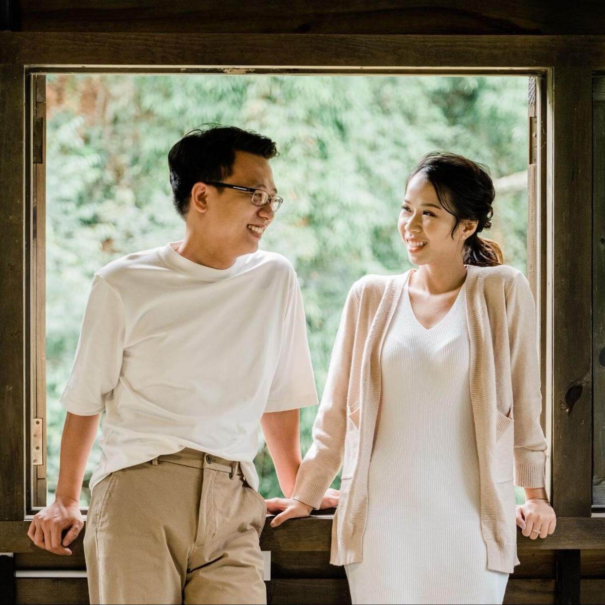 Young couple smiling at each other sitting by window with forest view in background