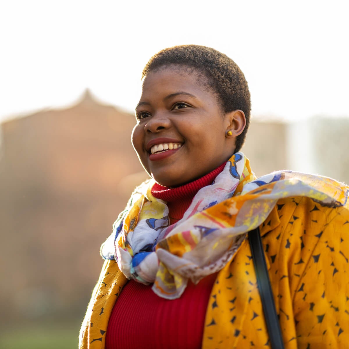 Smiling woman in red turtleneck and yellow patterned jacket with colorful scarf outdoors