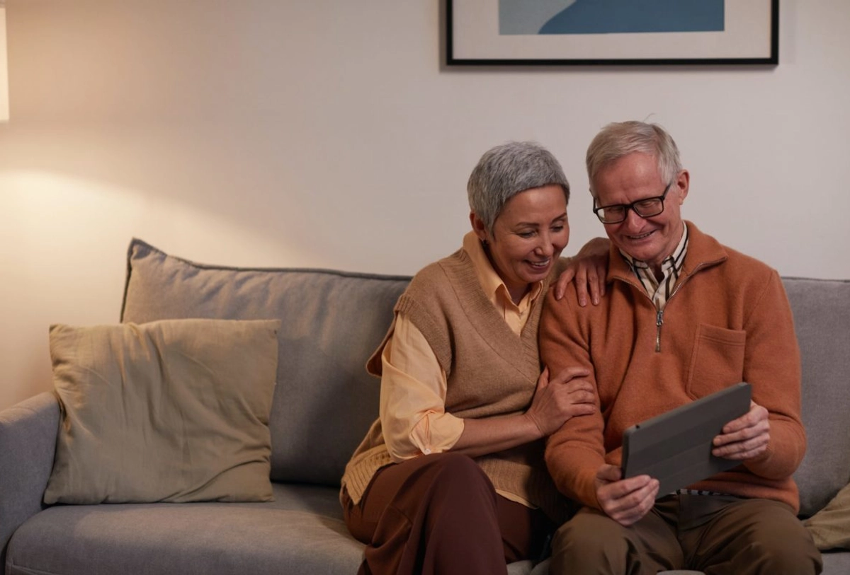 Senior couple smiling while viewing tablet together on gray couch at home