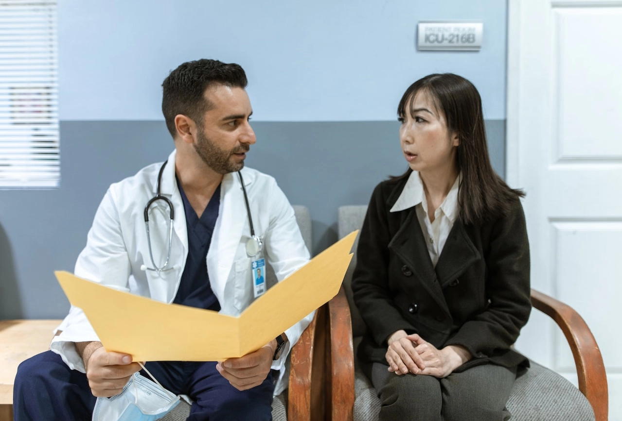 Doctor in white coat discussing patient file with woman in medical examination room