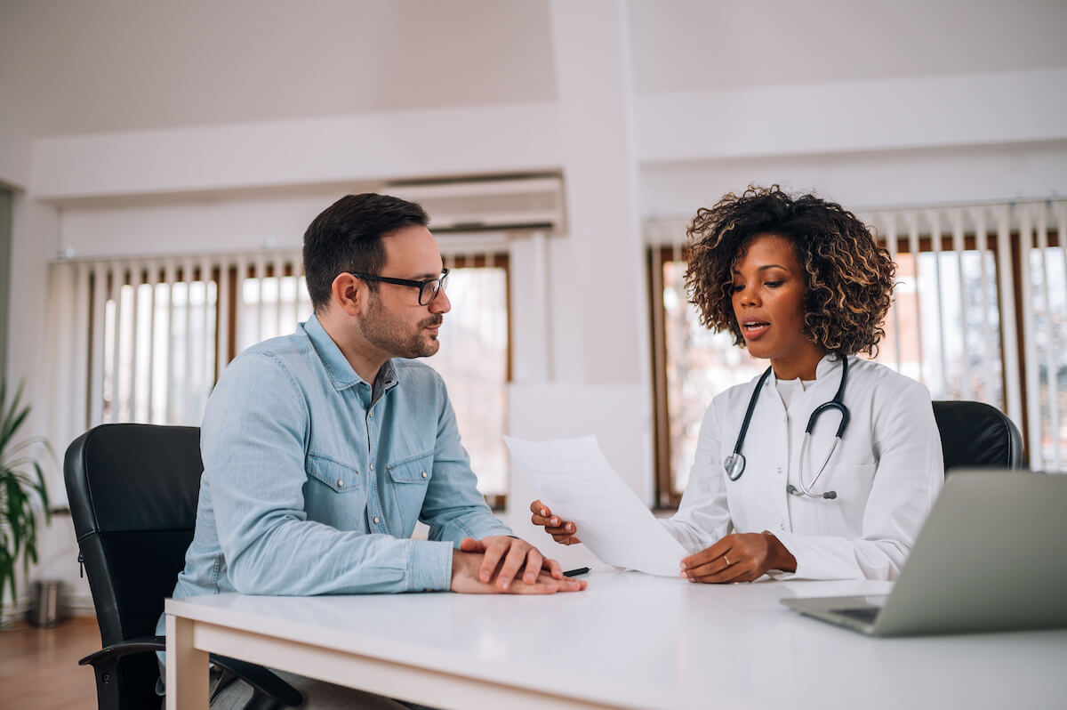 Female doctor consulting with male patient at desk in bright modern medical office with laptop