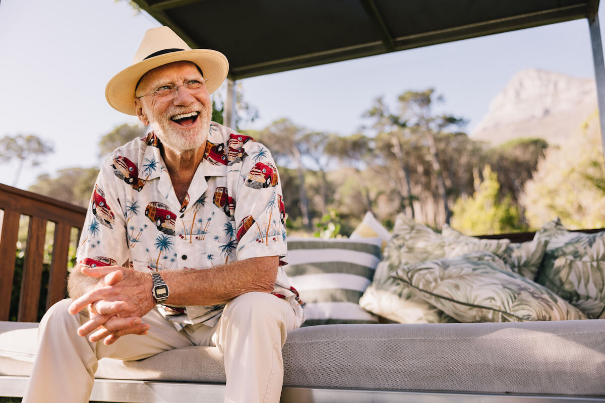 Happy senior couple laughing outdoors with woman on man's back, green trees in blurred background