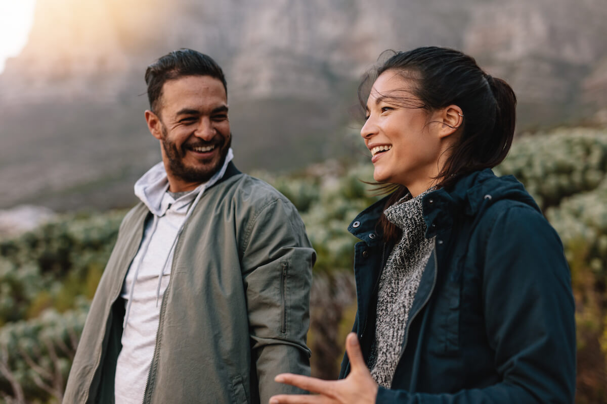 Couple smiling and talking outdoors with mountains and forest in background