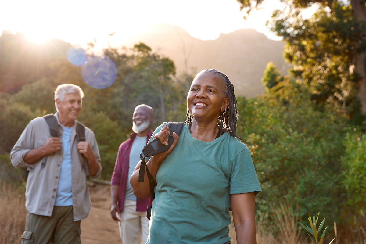Group of people hiking on mountain trail at sunset with woman in teal shirt leading