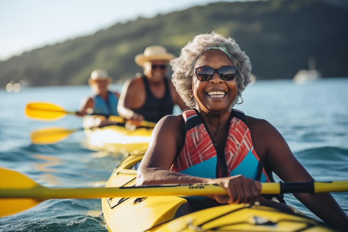 Smiling senior with sunglasses kayaking in yellow boat on blue water, others paddling in background.