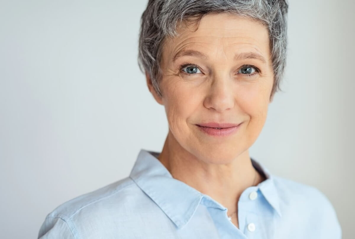 Older woman with short gray hair wearing light blue shirt smiling at camera