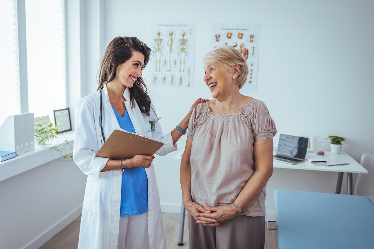 Doctor with clipboard and patient smiling during consultation in medical office with anatomical charts on wall