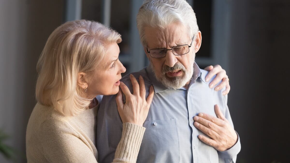 Concerned older woman supporting senior man experiencing chest pain or heart attack symptoms