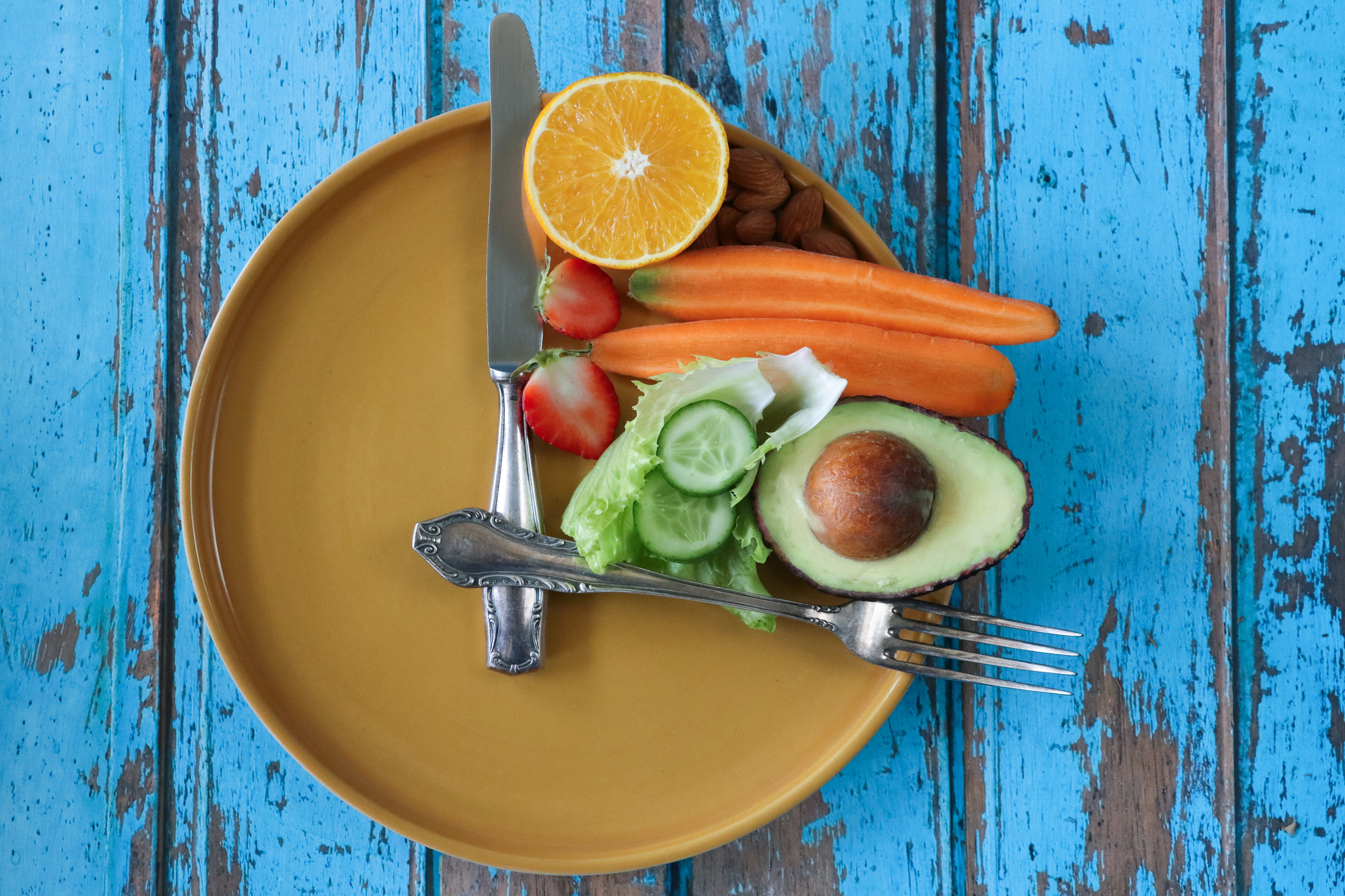 A plate of fruits and vegetable with the knife and fork placed ontop