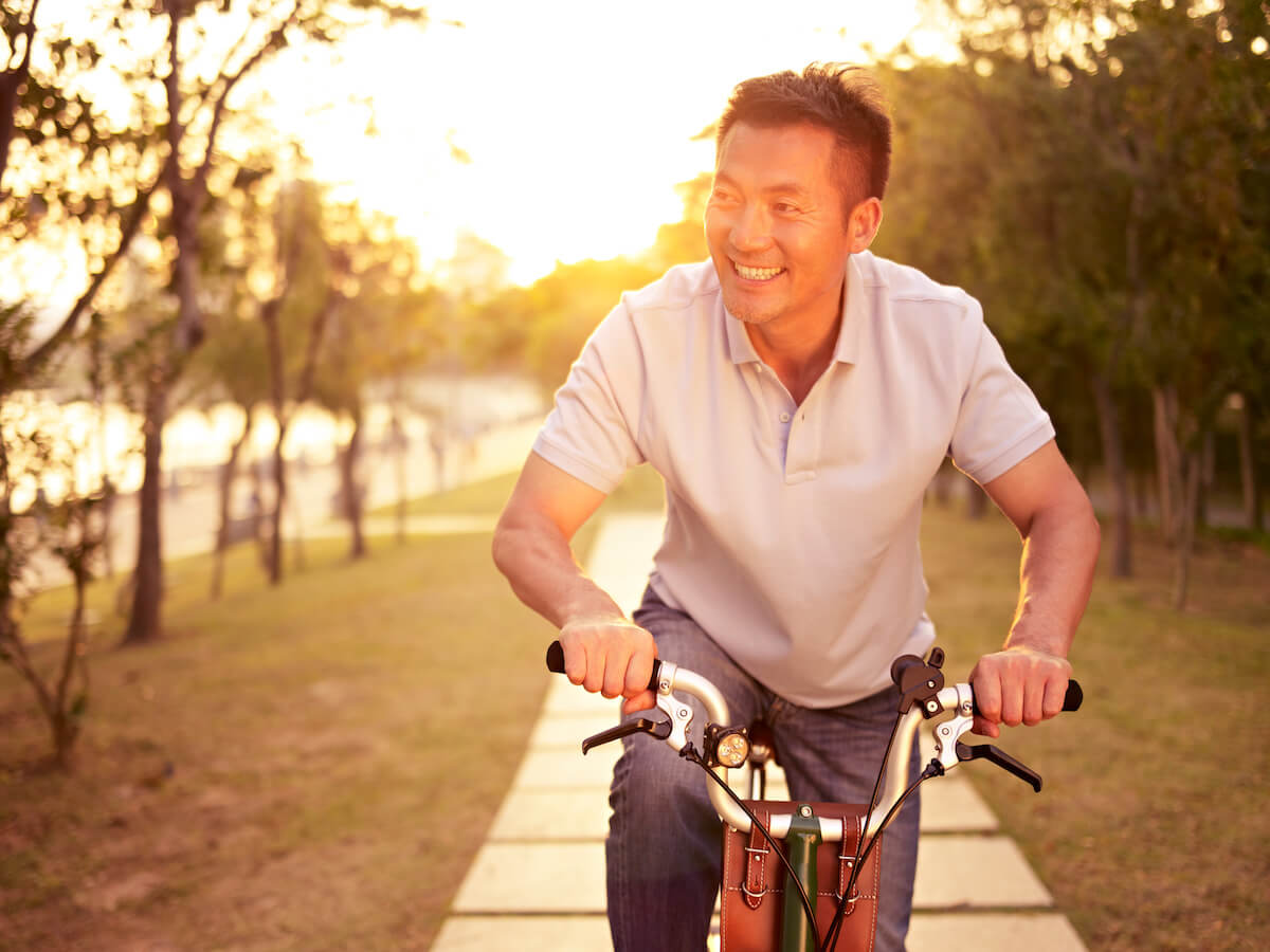 Man smiling while riding bicycle on tree-lined path at sunset