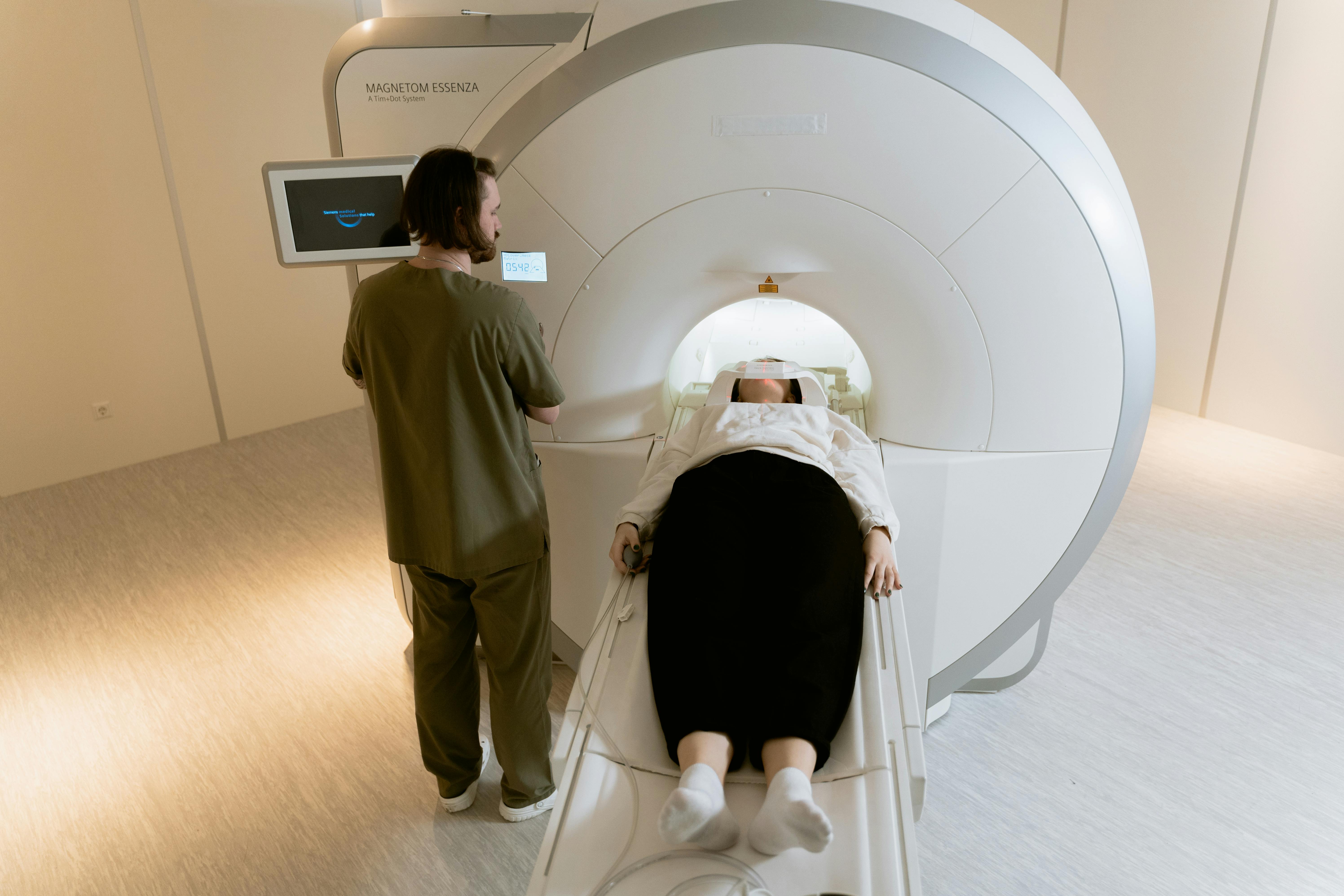 Medical technician operating MRI machine with patient on scanning table in clinical hospital setting