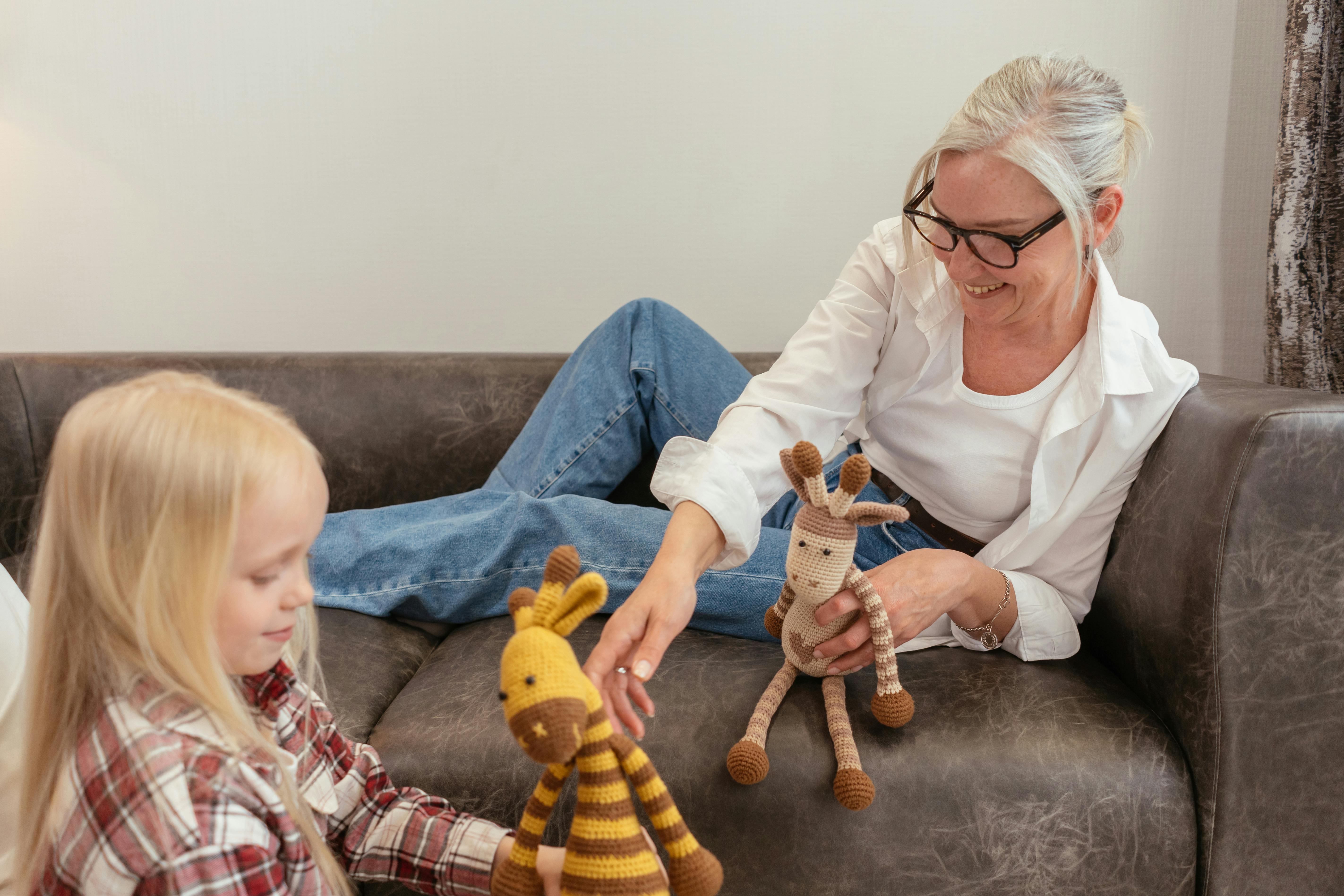 Woman and girl on couch with knitted stuffed animals, woman in white shirt and glasses, child in red plaid shirt