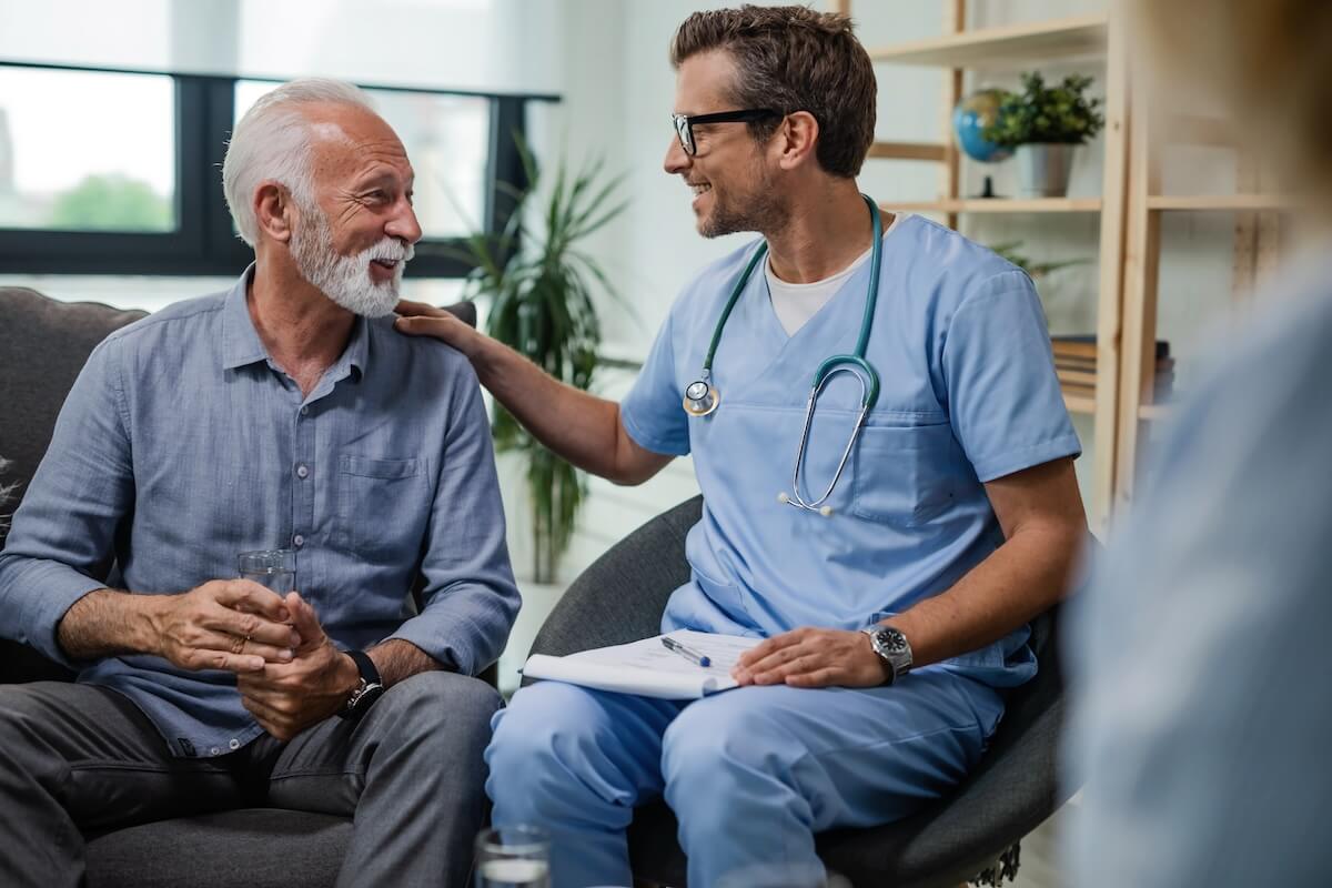 Healthcare provider in blue scrubs with stethoscope conversing with senior patient in bright medical office setting