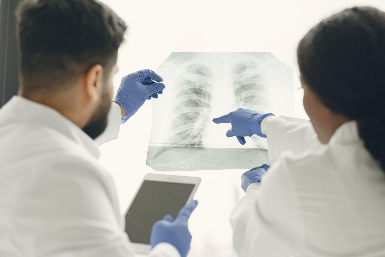 Two doctors in white coats and blue gloves examining chest x-ray with tablet device